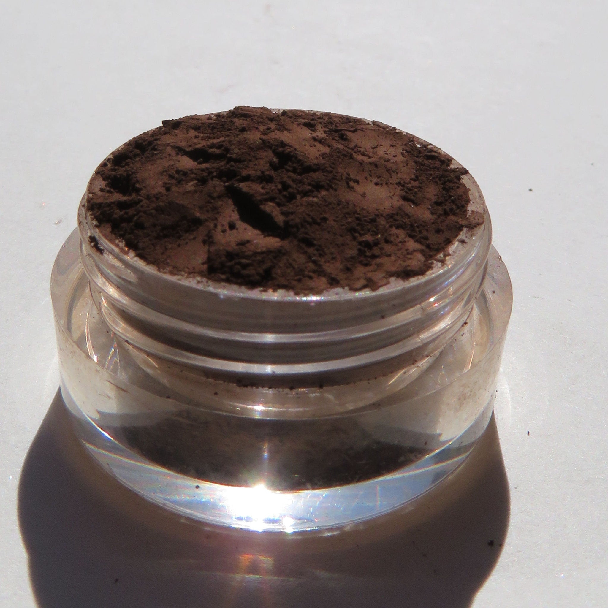 Close-up of matte brown mineral eye shadow powder spilling from jar onto textured surface
