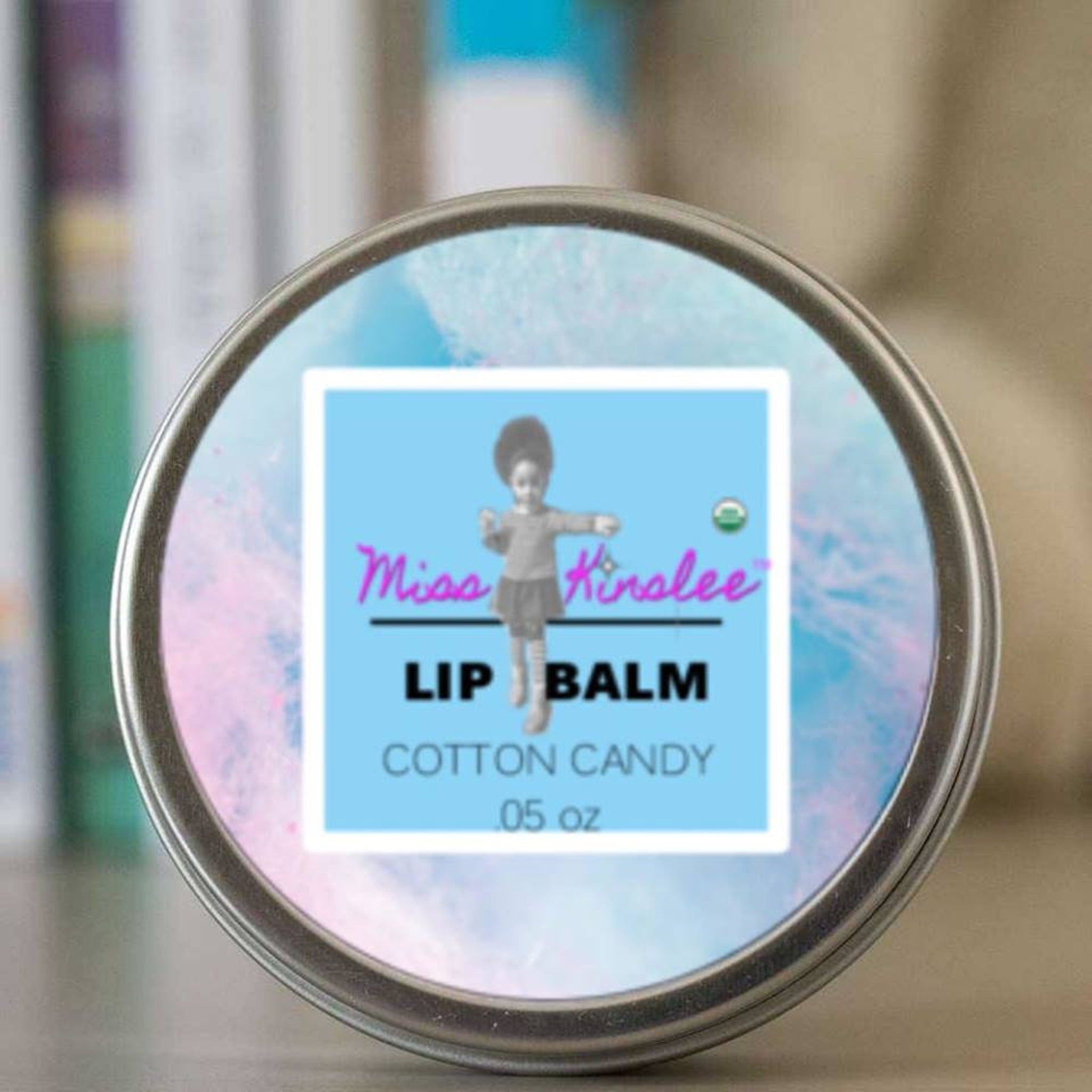 Lip balm tin with silver metal rim, blue and pink background, and Miss Kinslee label.