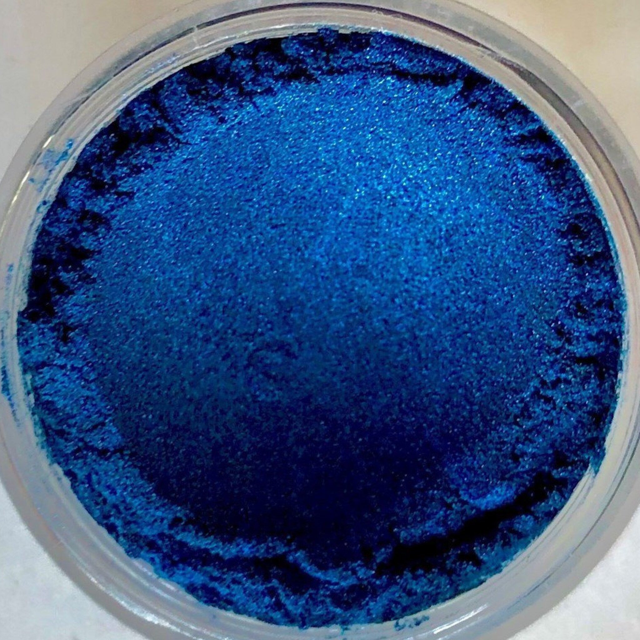 Close-up of dark blue metallic sapphire eye shadow powder with shimmering finish in compact case
