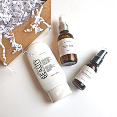 Facial skincare products in white, brown, and clear bottles on white surface with box and paper filler