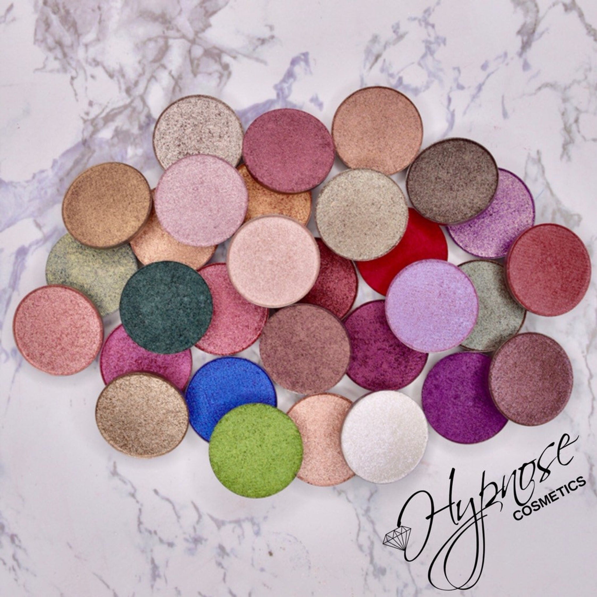 Eyeshadow palette with various colors, round shape, and Hypnose Cosmetics logo on marble background