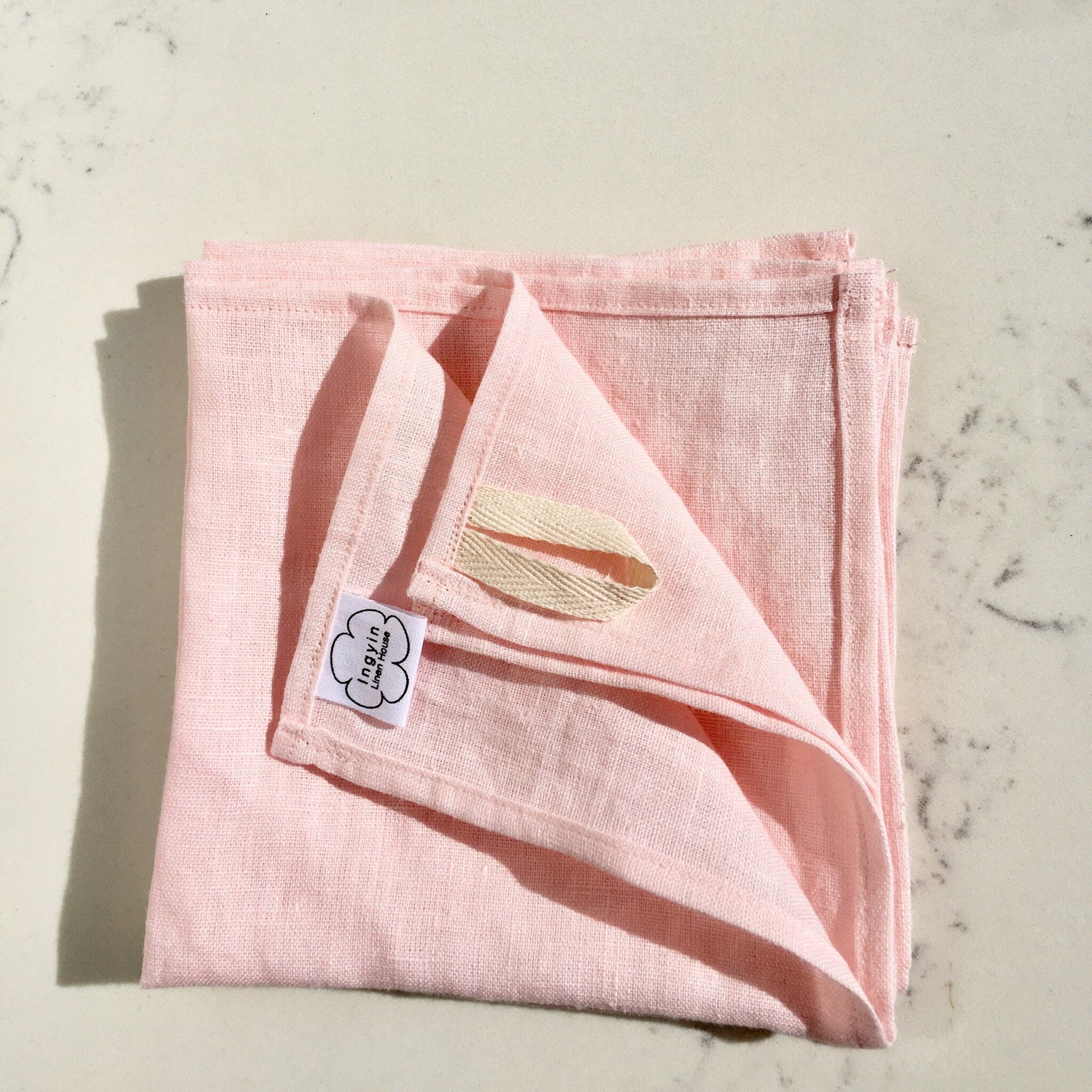 Pink linen cloth with visible weave and Ingyin Linen House label, folded on marble surface