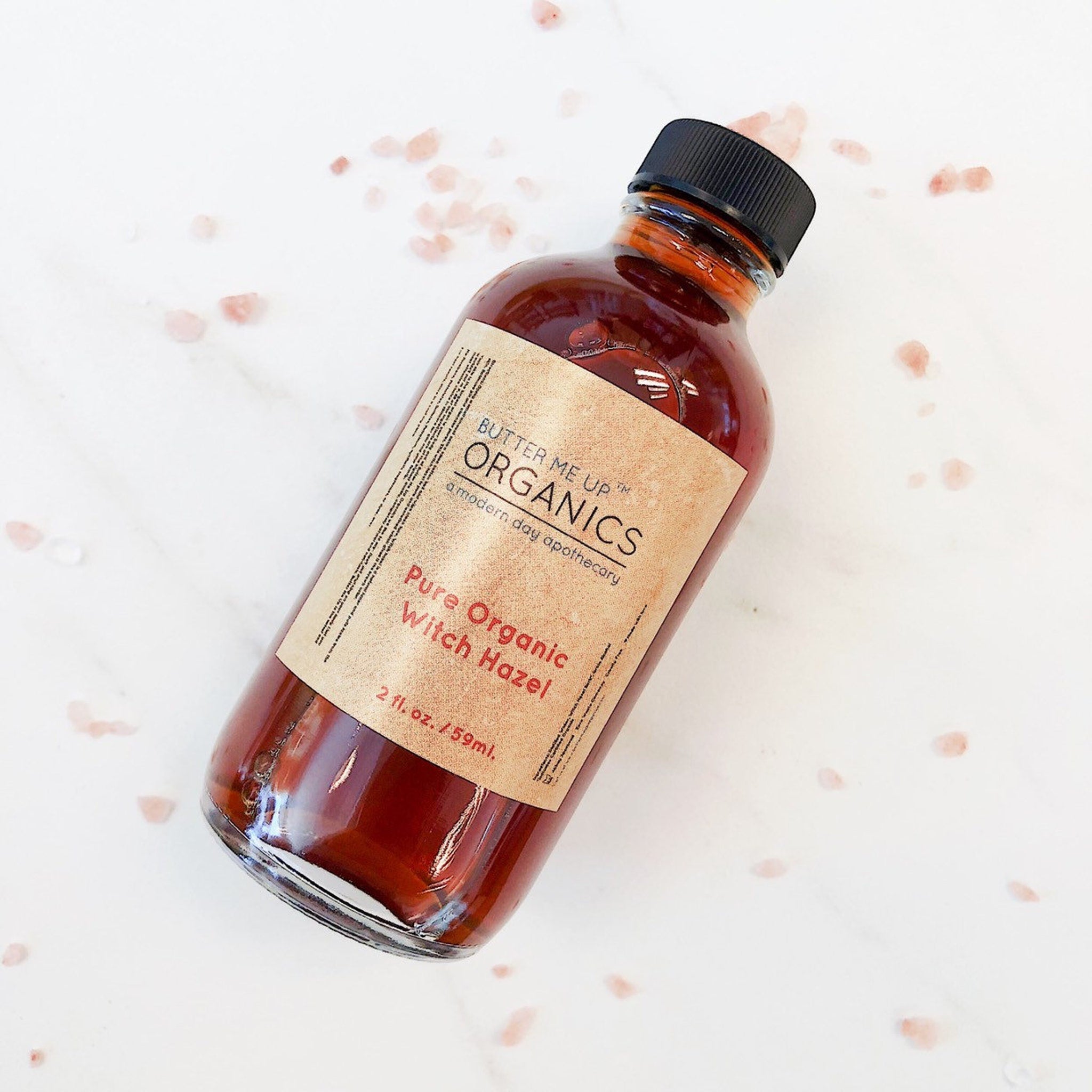 Witch hazel bottle with brown liquid, black cap, and paper label, Butter Me Up Organics brand