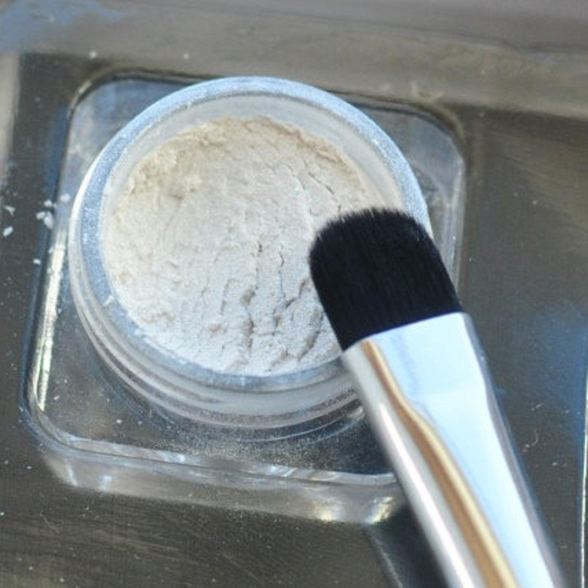 Powder makeup in clear jar with black brush, light beige color, close up view