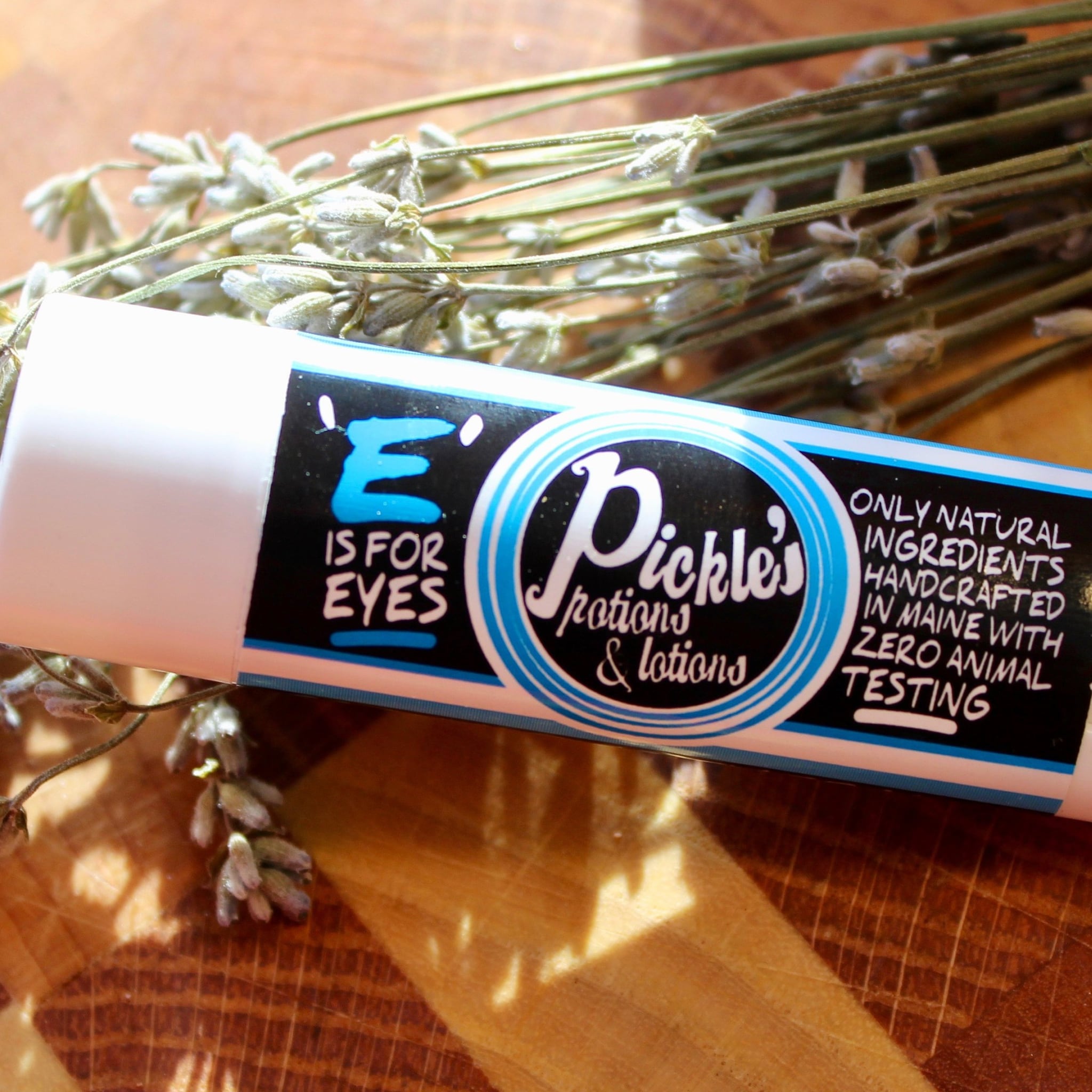 Eye product tube with white, blue, and black label, "Pickle's" brand, and lavender sprigs on wood surface