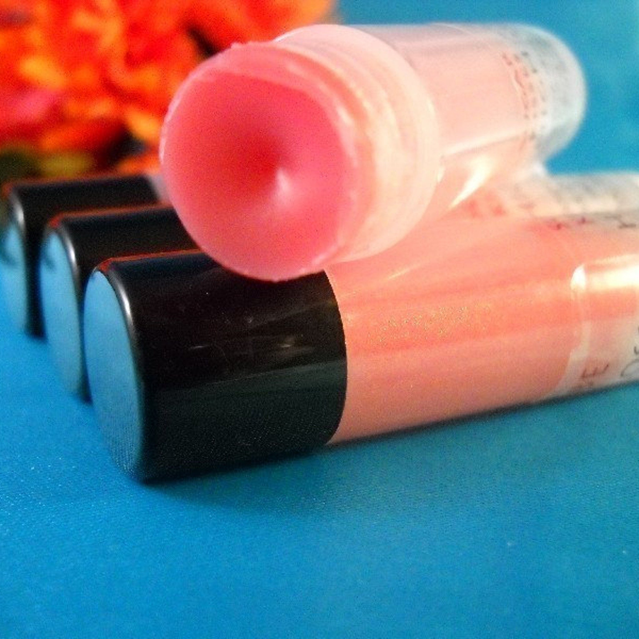 Lip gloss tubes with pink gloss, black caps, and clear plastic packaging