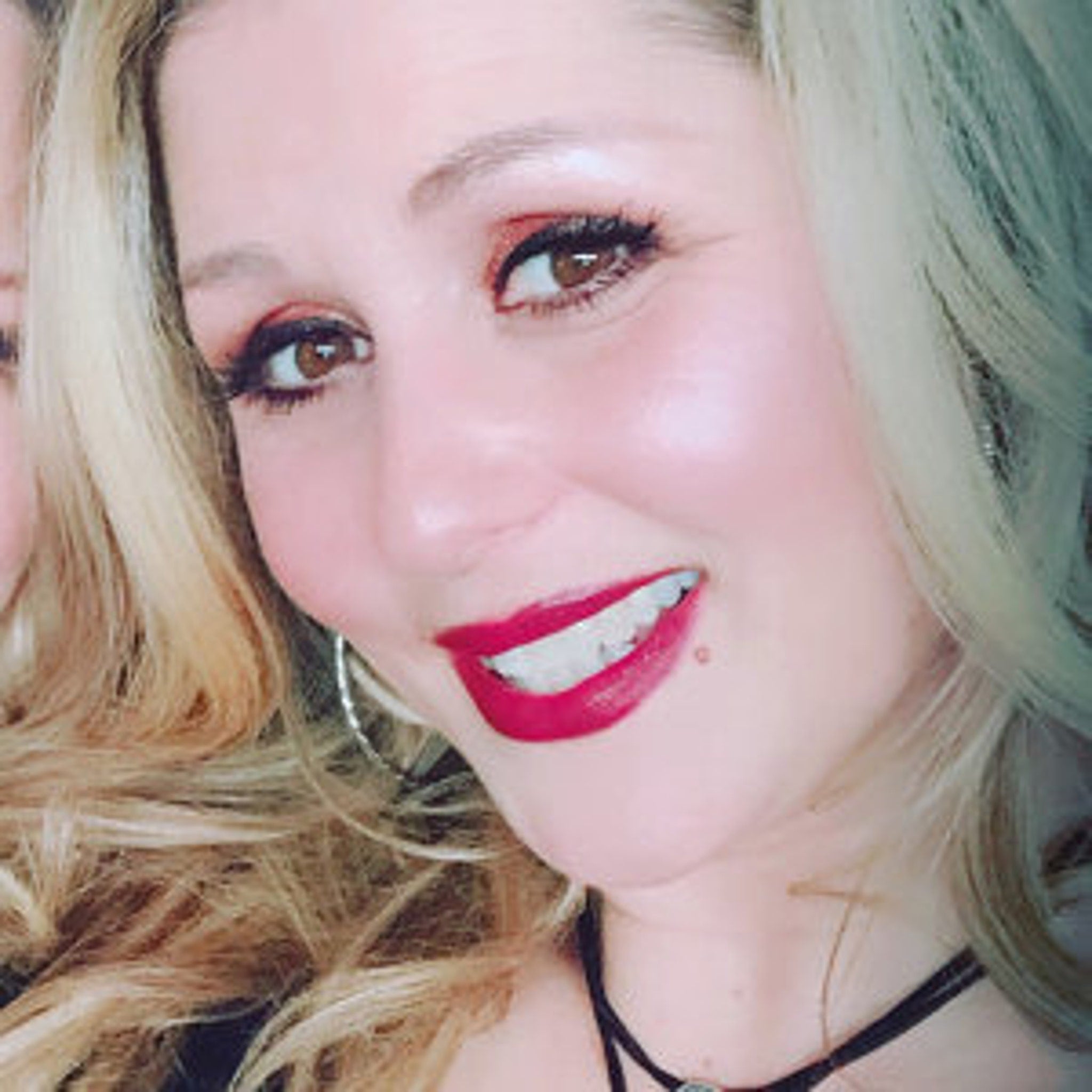 Woman with blonde hair, red lipstick, and silver hoop earrings smiling at camera