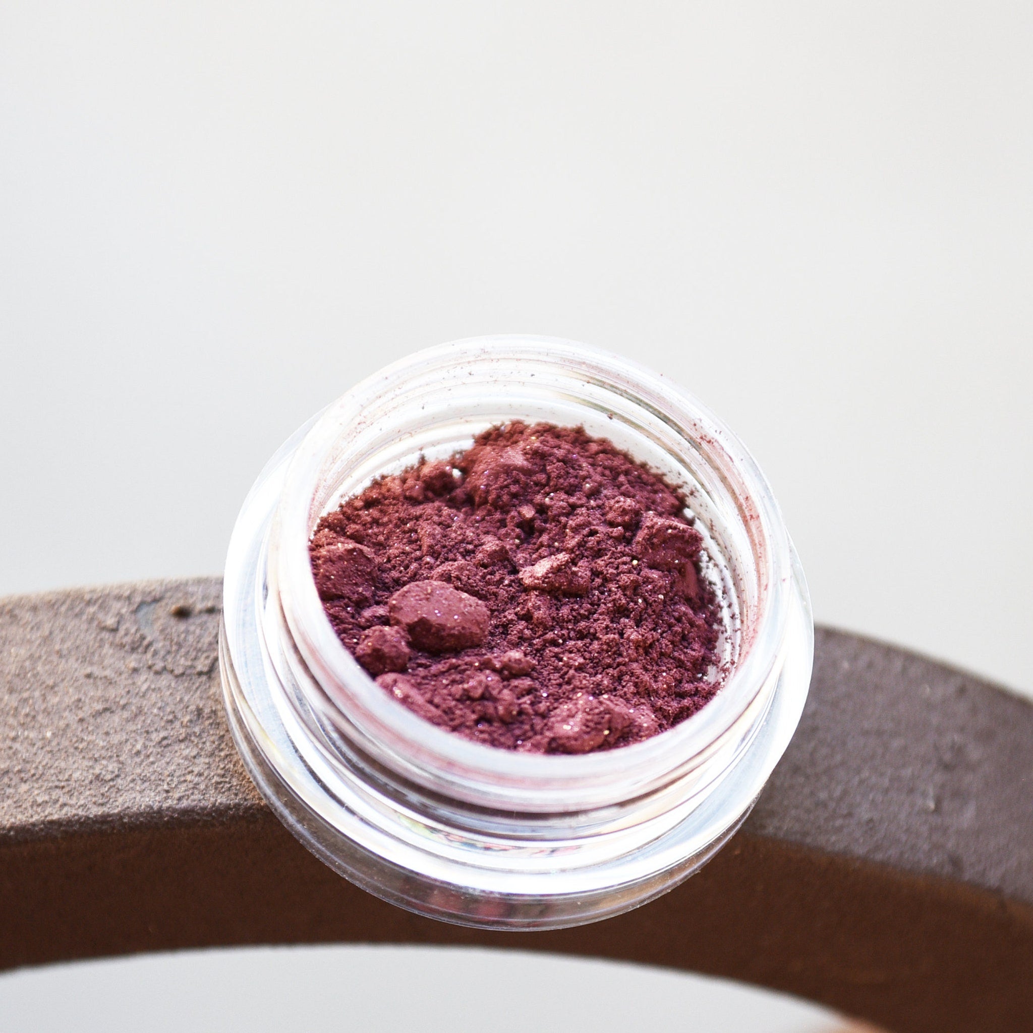 Close-up of pigmented mineral eye shadow in a jar with sifter, showcasing vibrant color and fine powder texture