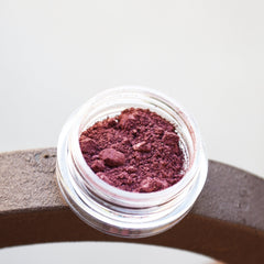 Close-up of pigmented mineral eye shadow in a jar with sifter, showcasing vibrant color and fine powder texture