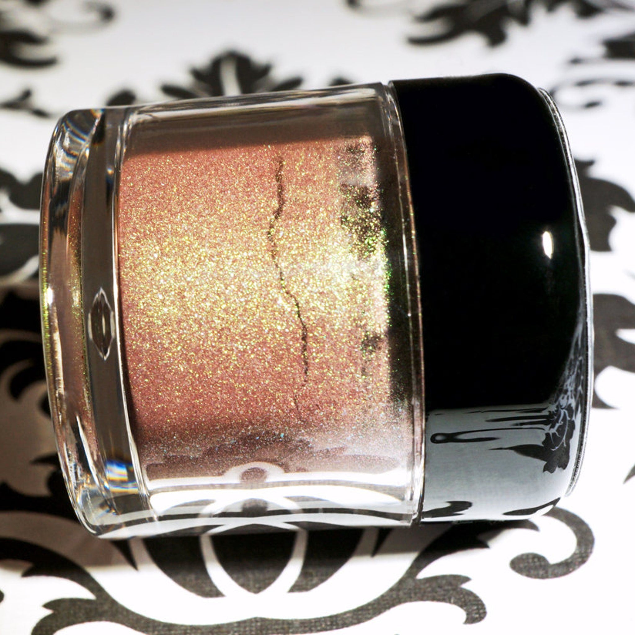 Side view of duochrome green-brown eyeshadow pan showing burgundy base with iridescent shimmer shift