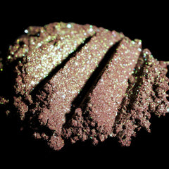 Side angle of duochrome green-brown eyeshadow pan catching light to reveal burgundy and iridescent shimmer shift