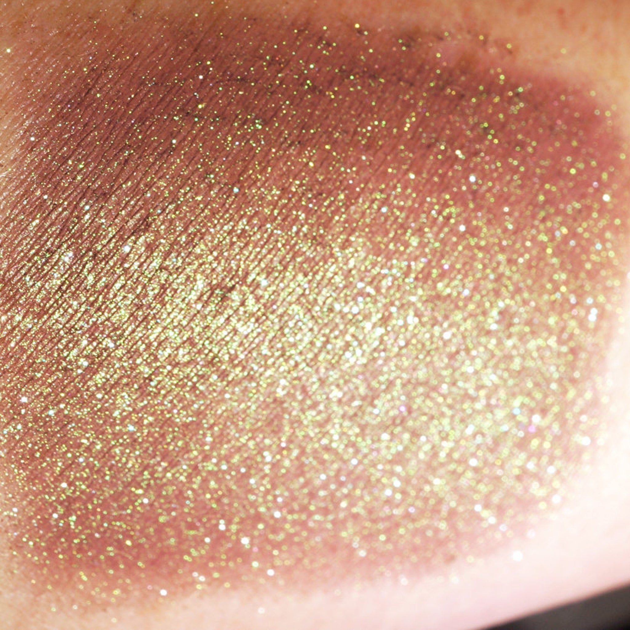 Side view of duochrome green-brown eyeshadow pan catching light to reveal burgundy and iridescent shimmer shift