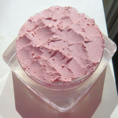 Pastel pink loose powder eyeshadow in a transparent jar with black screw-top lid and seashell design on label