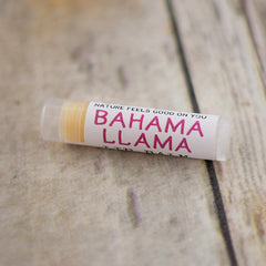 Lip balm tube with white label, pink text, and clear plastic casing on wood surface