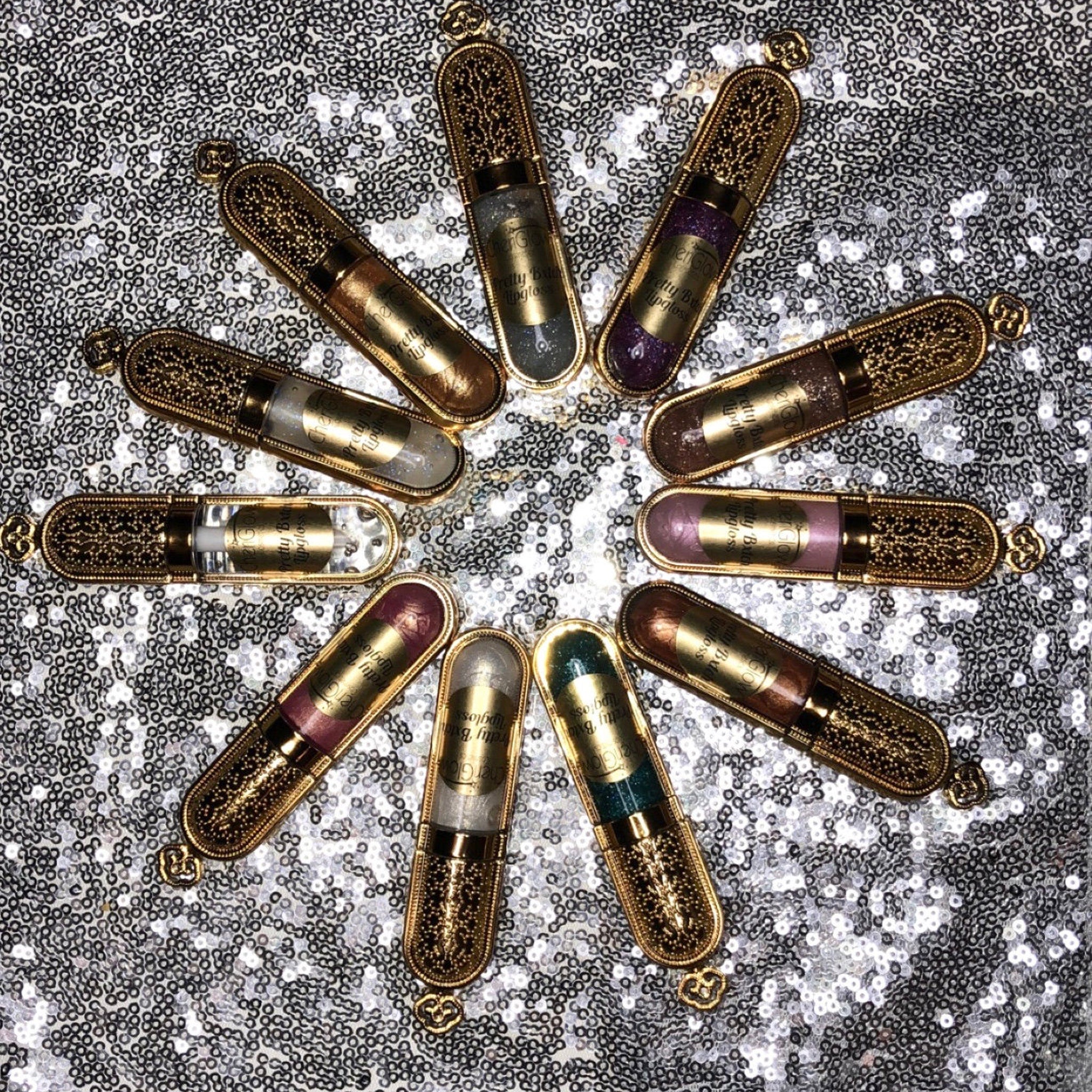 Lip gloss tubes with gold filigree cases, various colors, and "CherGlow" text on a sequin background