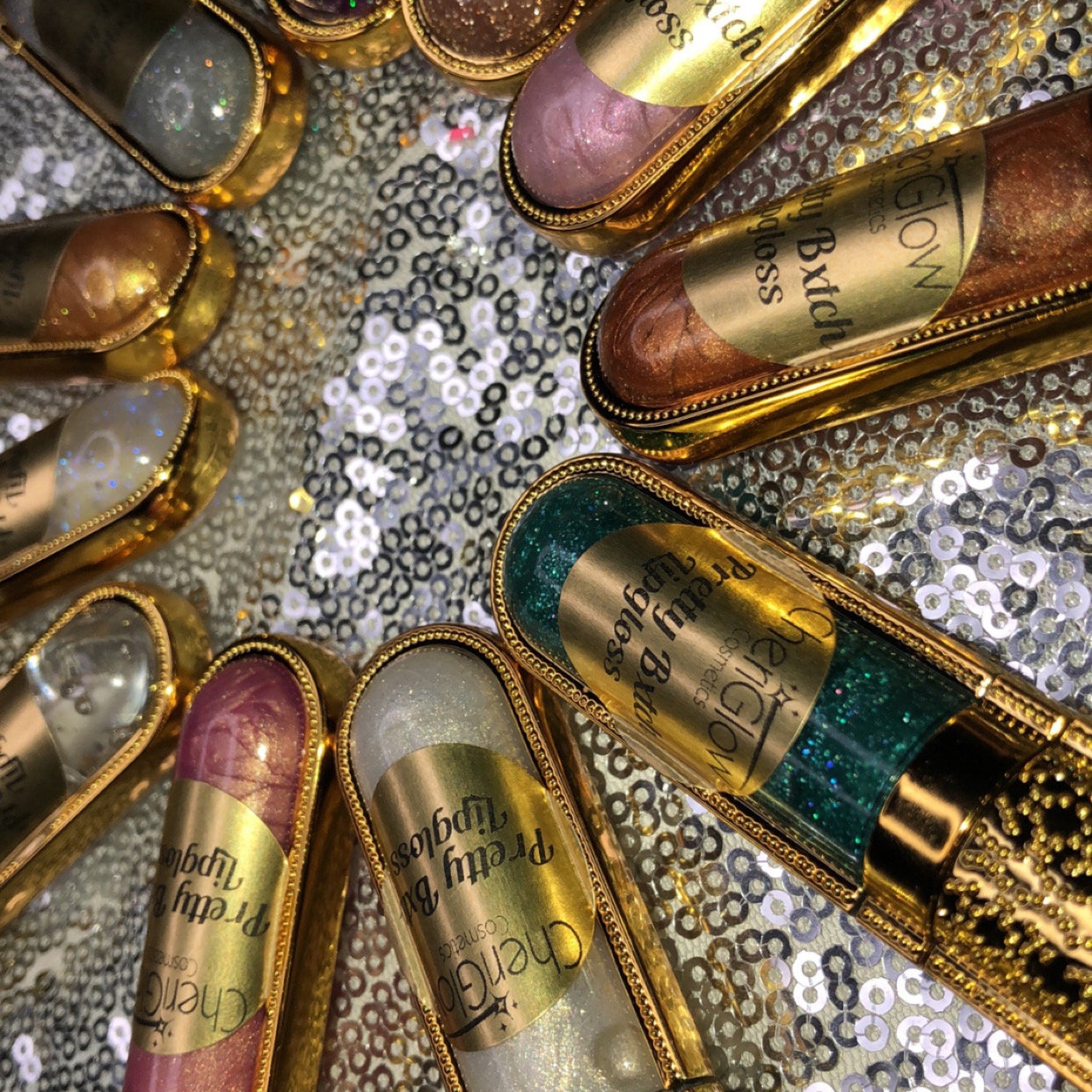 Lipgloss tubes with gold trim, glittery colors, and "CherGlow" label on shiny background