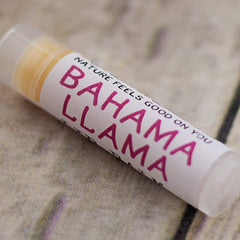 Lip balm tube with white label, pink text "Bahama Llama", and clear cap on a patterned surface