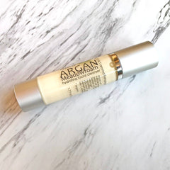 Facial cleanser bottle with silver cap, cream-colored liquid, and "Argan Meadowfoam" text on a marble surface.