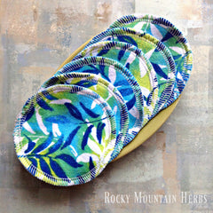 Reusable cotton facial rounds, blue and green leaf pattern, white stitched edge, on a plate