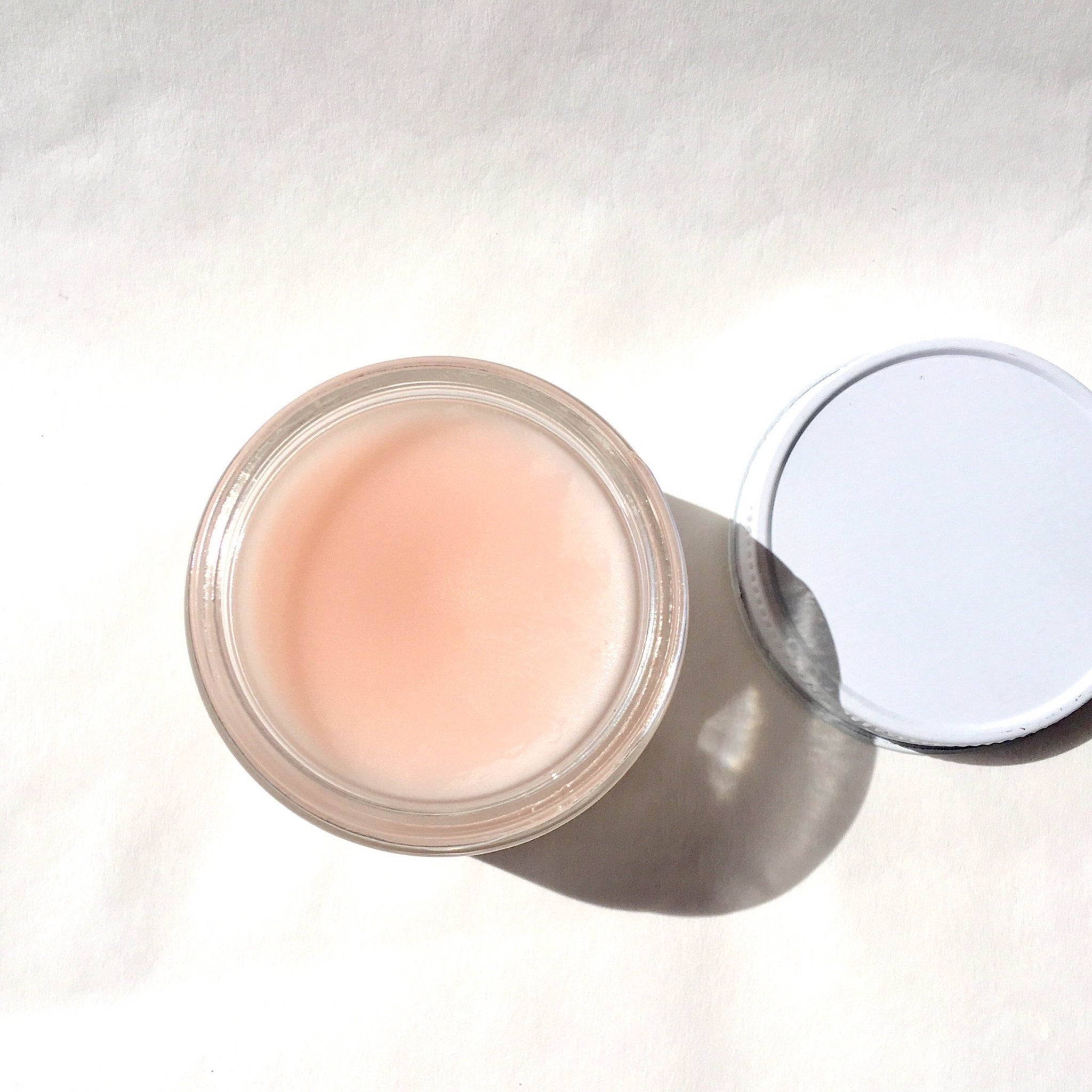 Lip balm in glass jar with pink balm and white lid on white surface