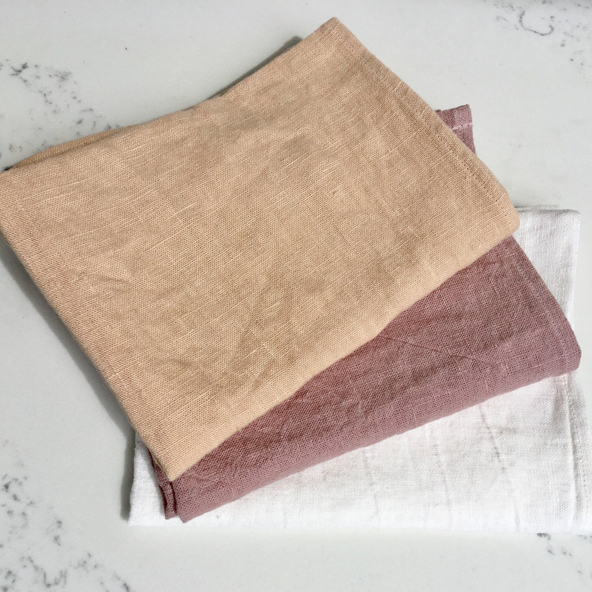 Cloth napkins in beige, mauve, and white linen fabric, folded and stacked
