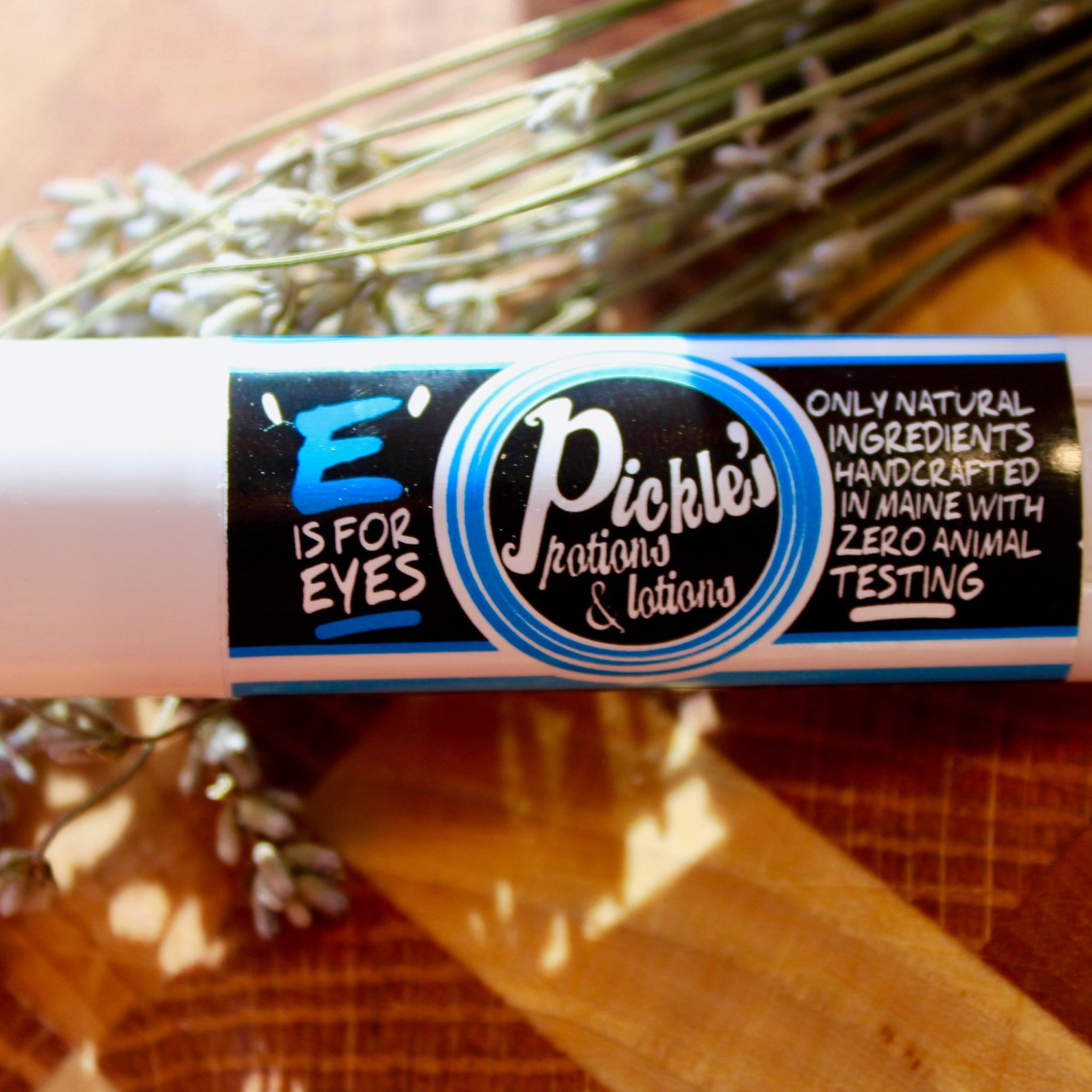 Eye product with white tube, black and blue label, and "Pickle's" brand text with lavender sprigs in background