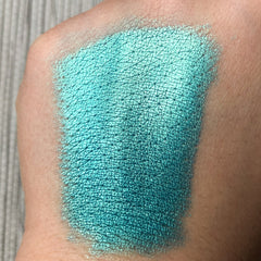 Close-up of fingertip applying shimmery azure blue eye shadow pigment to eyelid