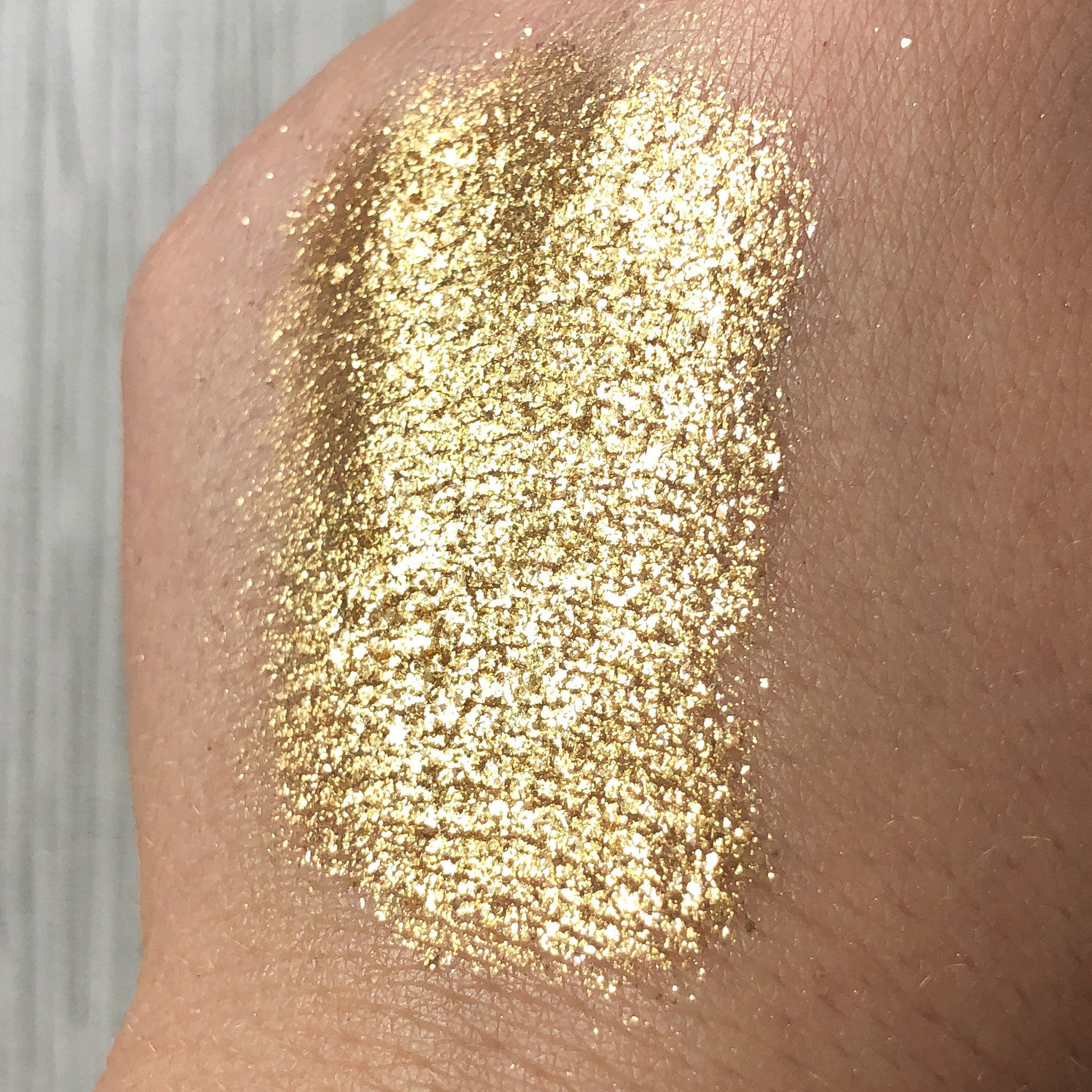 Gold glitter swatch on skin, showing texture and color, with light reflecting off the particles