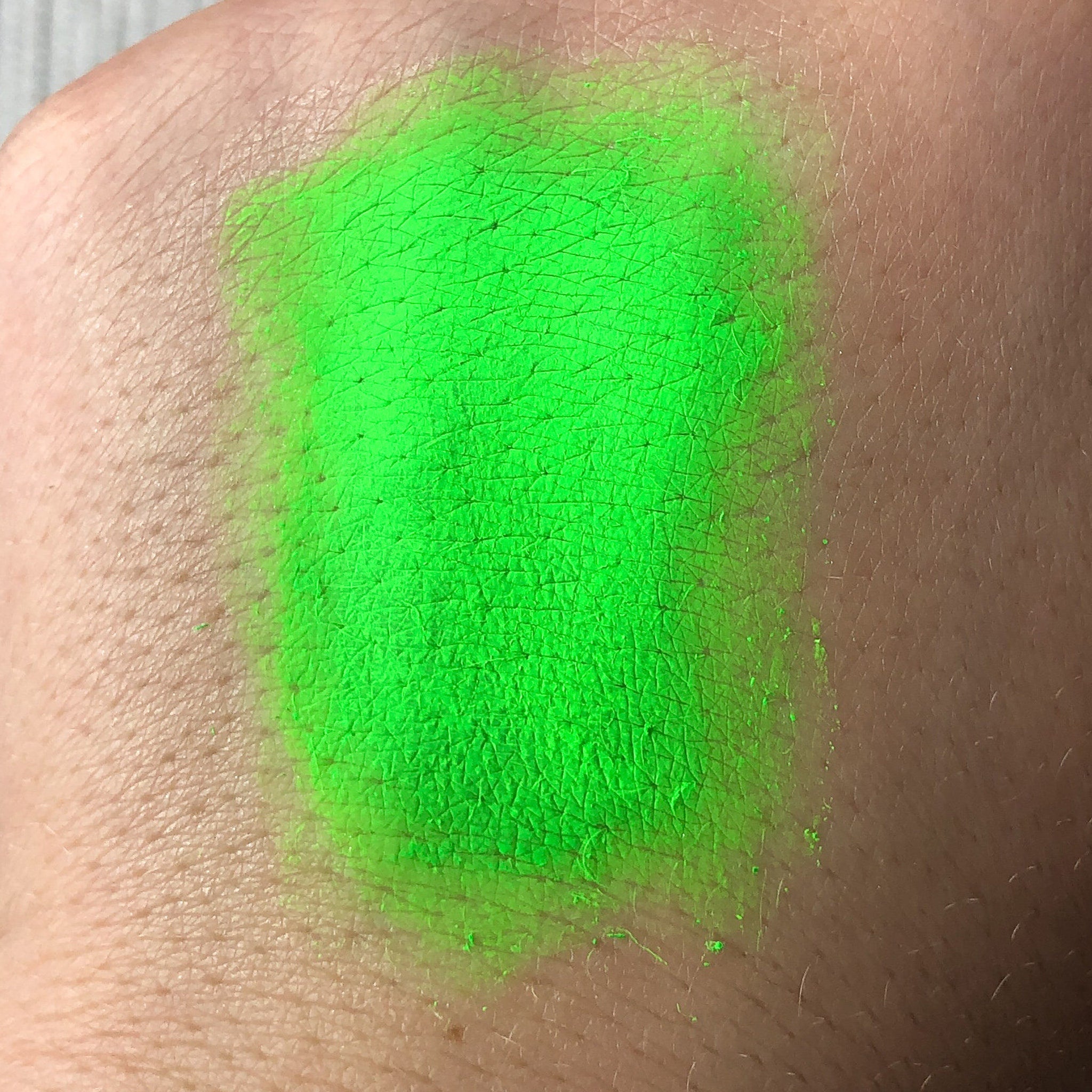 Green pigment swatch on skin, bright neon green color, textured application