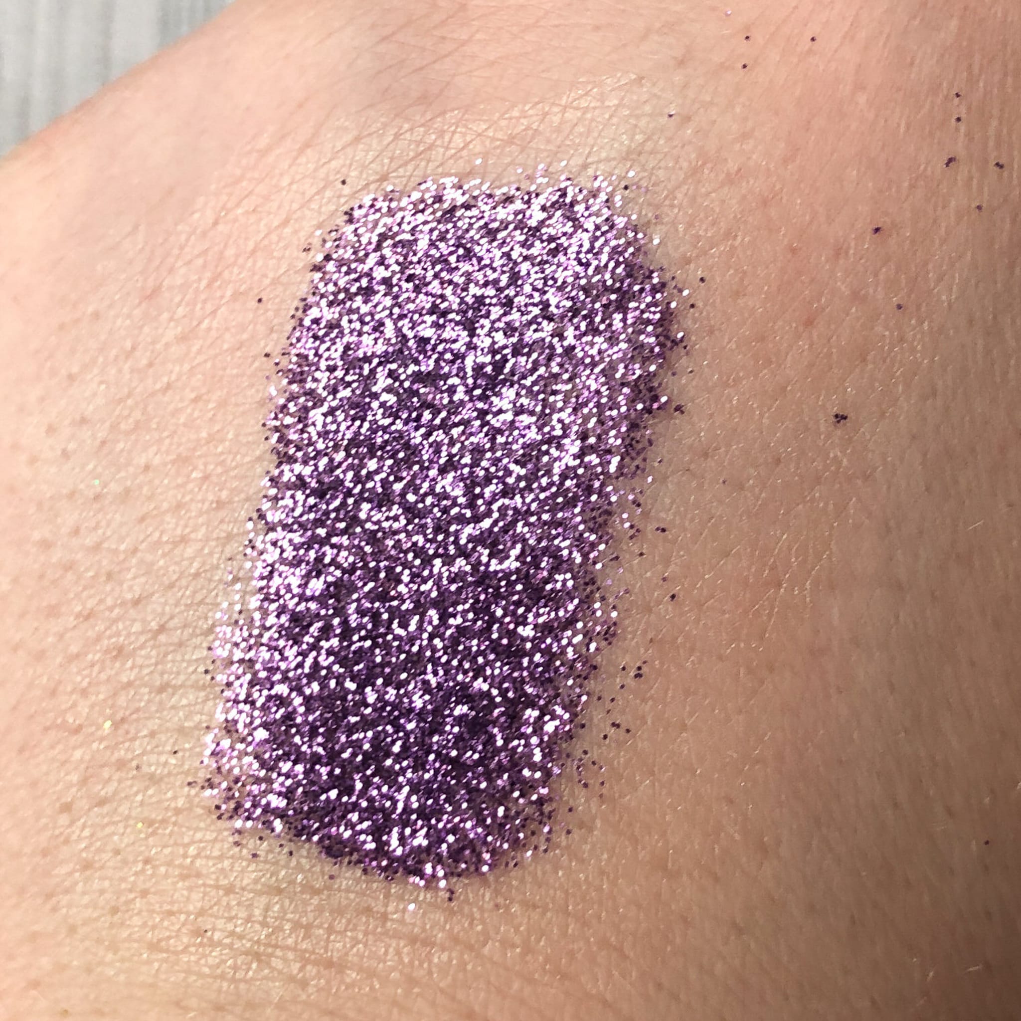 Purple glitter swatch on skin, showing fine particles and texture detail