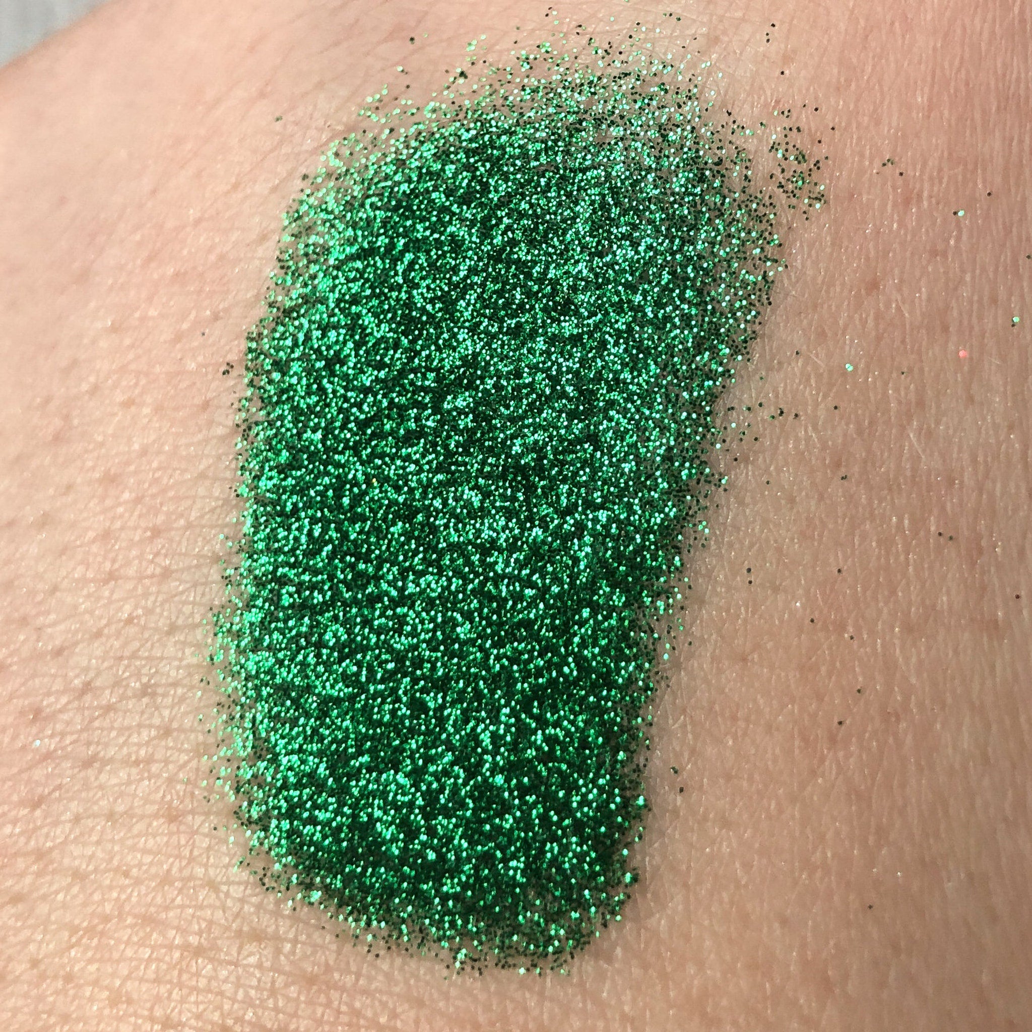 Green glitter eyeshadow swatch on skin, showing texture and sparkle