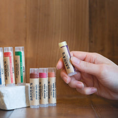 Tinted lip balm tubes with clear plastic, beige paper label, and Sasha's brand name, held in hand