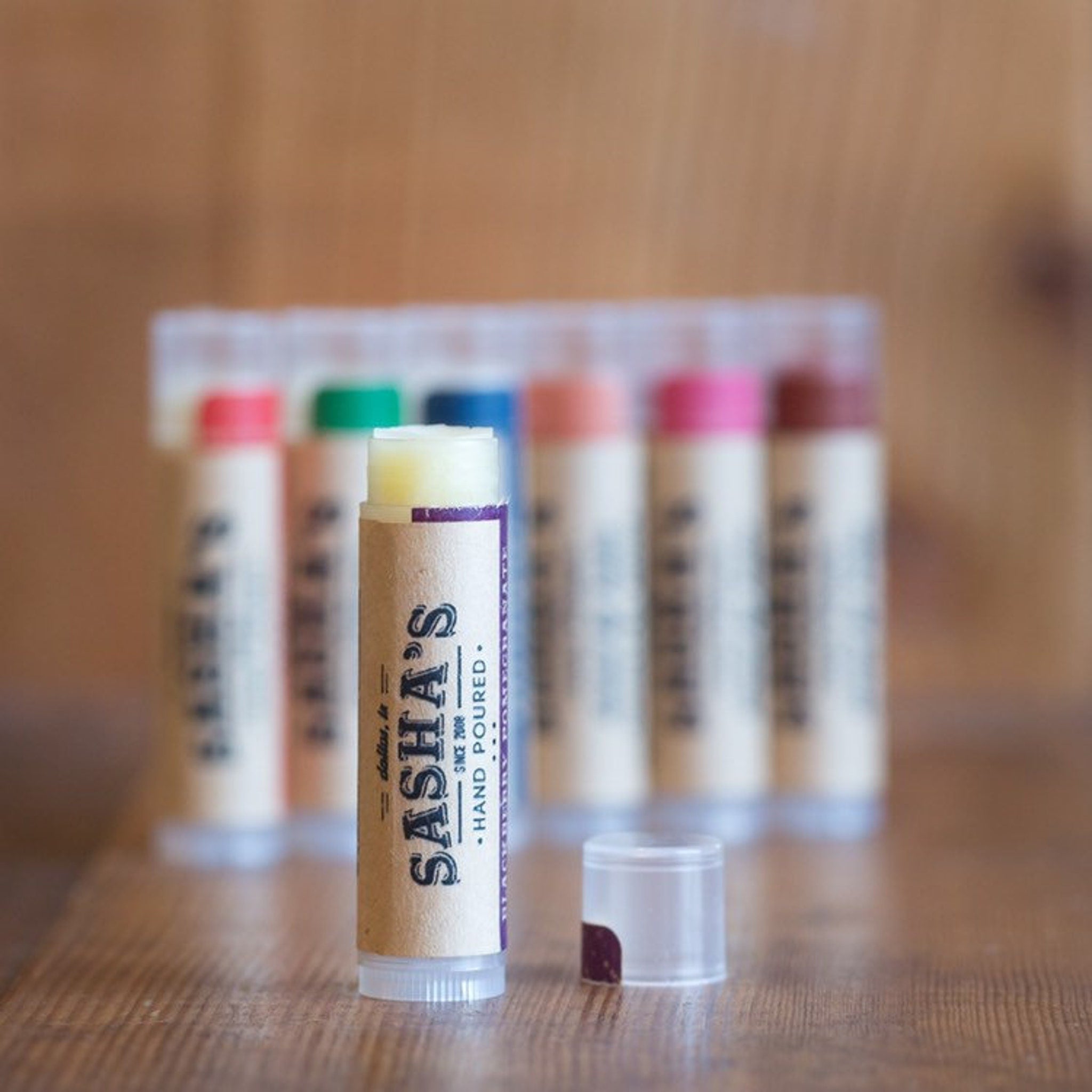 Lip balm tubes with brown paper labels, purple accents, and Sasha's brand text visible