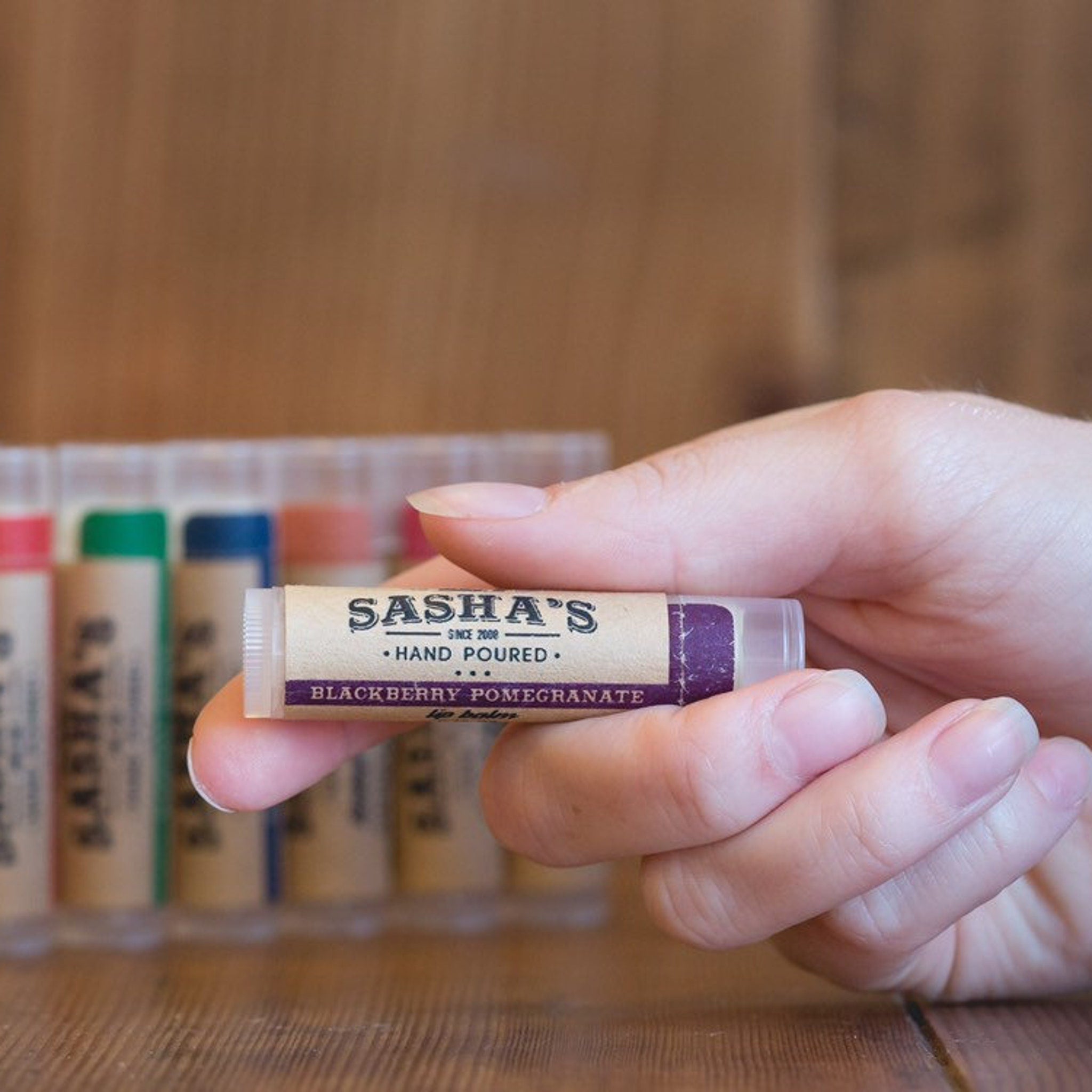 Lip balm tube with Sasha's label, clear plastic, purple label detail, held in hand