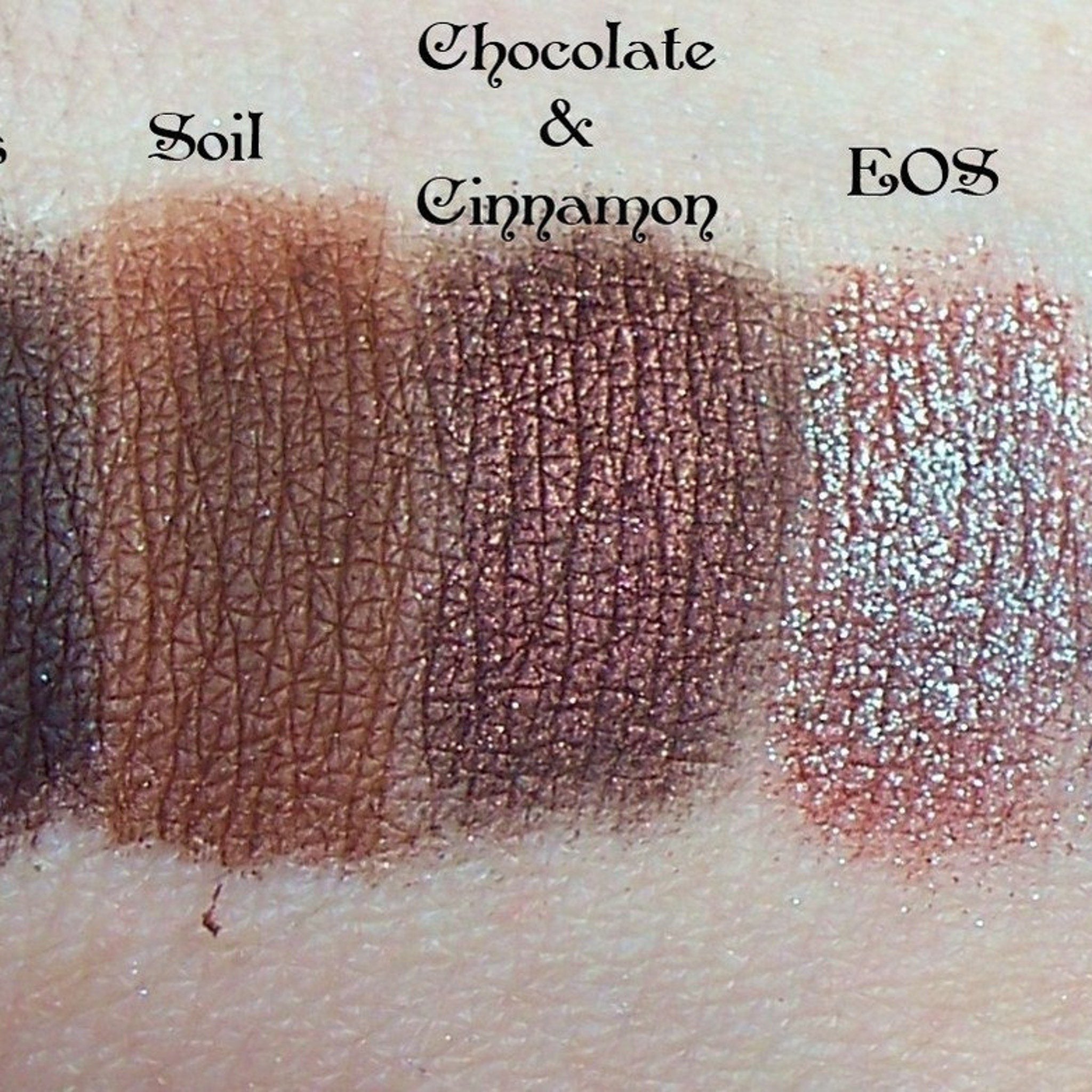 Side view of duochrome eyeshadow pigment pots in brown, red, green, and blue showing metallic sheen