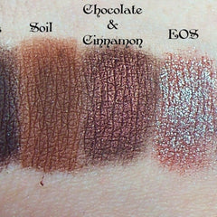 Side view of duochrome eyeshadow pigment pots in brown, red, green, and blue showing metallic sheen