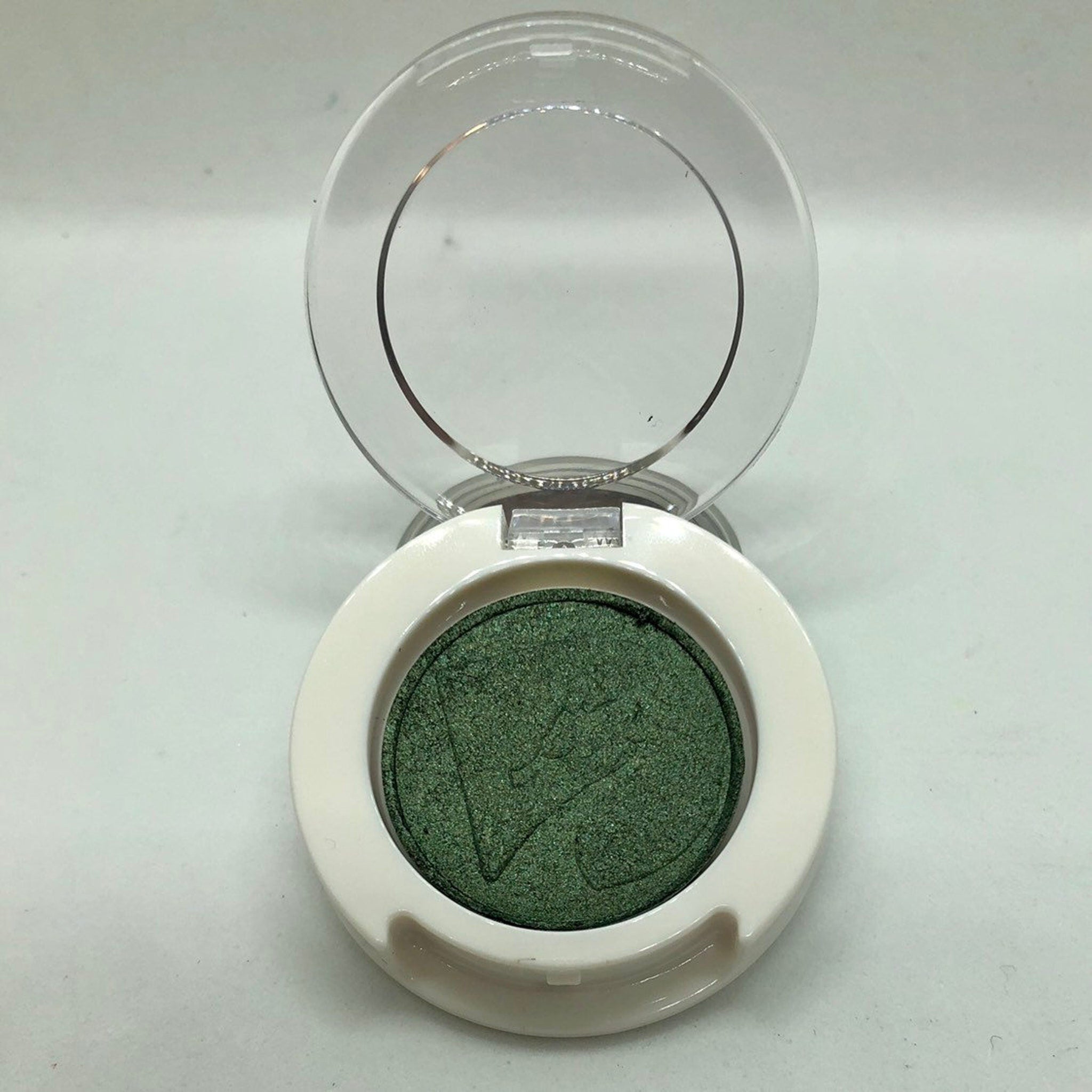 Green eyeshadow with white compact and clear lid open, makeup product