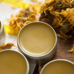 Lip balm tin with yellow balm, silver metal container, and dried flowers nearby