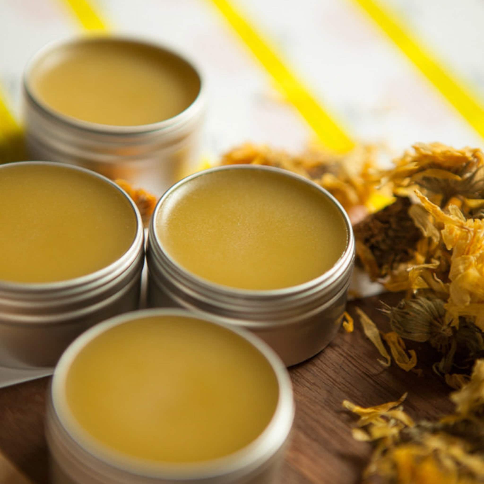 Balm tins with yellow balm, silver metal containers, and dried flowers on wood surface