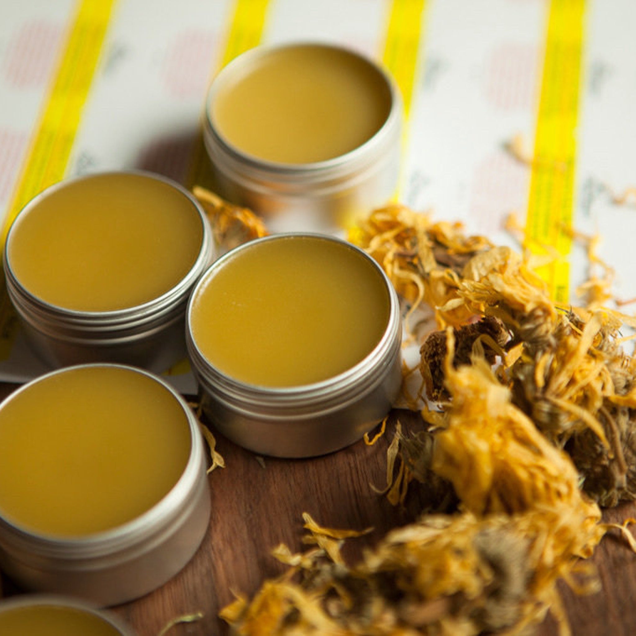 Balm in metal tins with yellow contents and dried flowers on wood surface