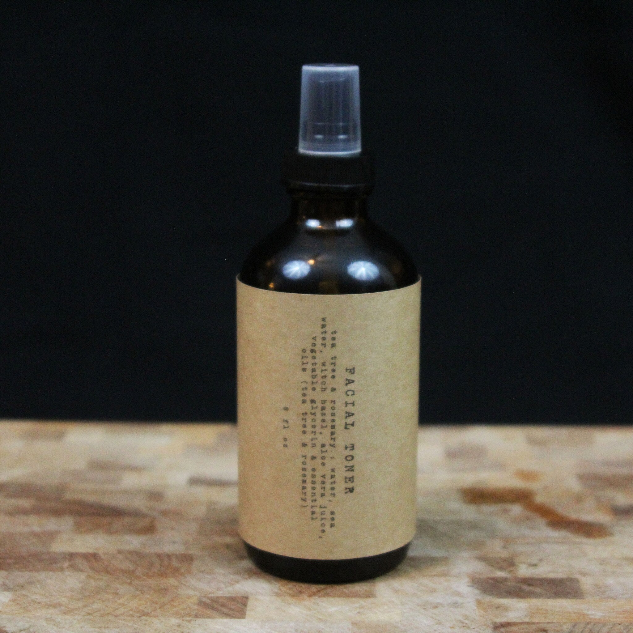 Facial toner bottle with brown glass, beige label, and clear spray top on wood surface