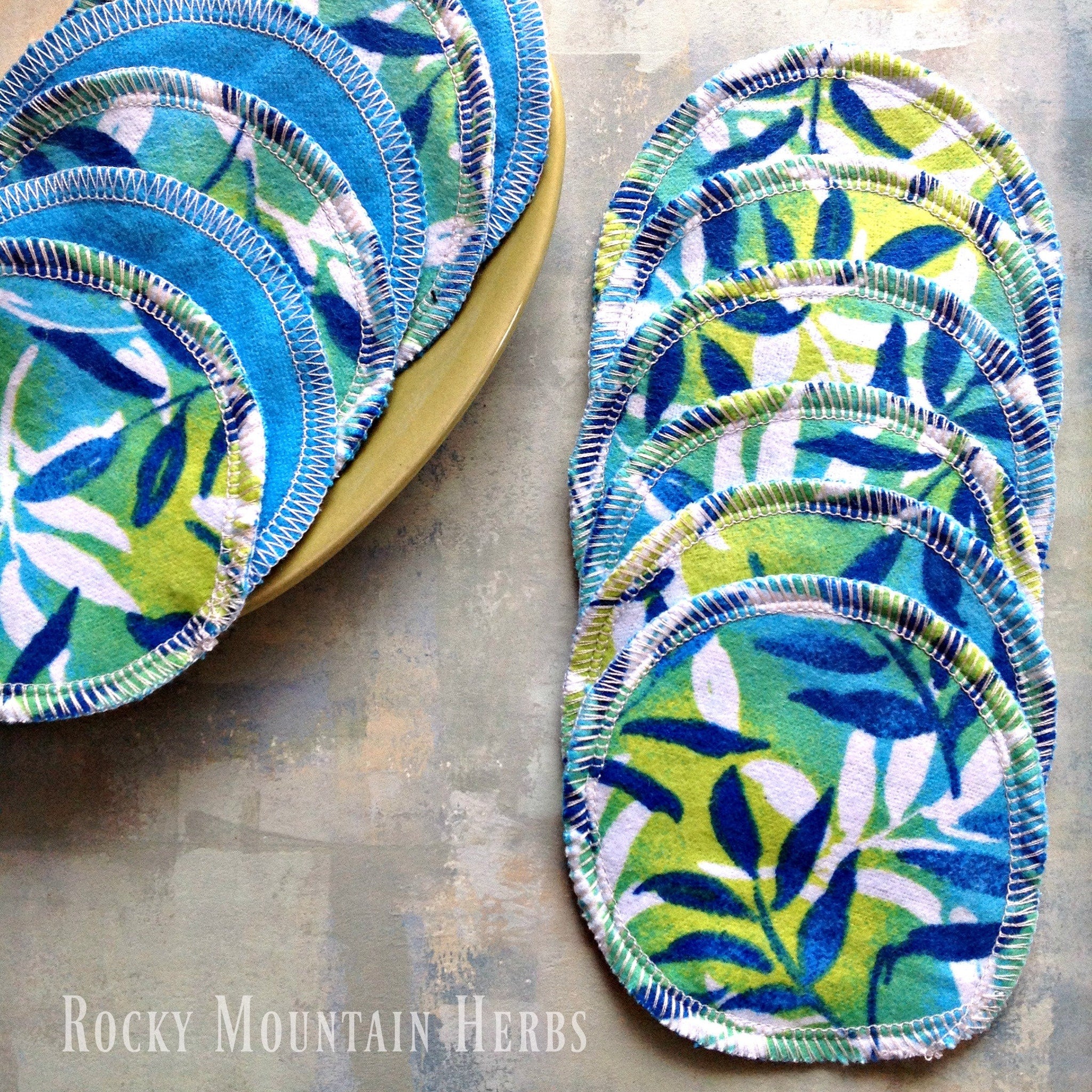 Reusable pads with blue, green, and white floral pattern, white stitched edges, and "Rocky Mountain Herbs" text visible