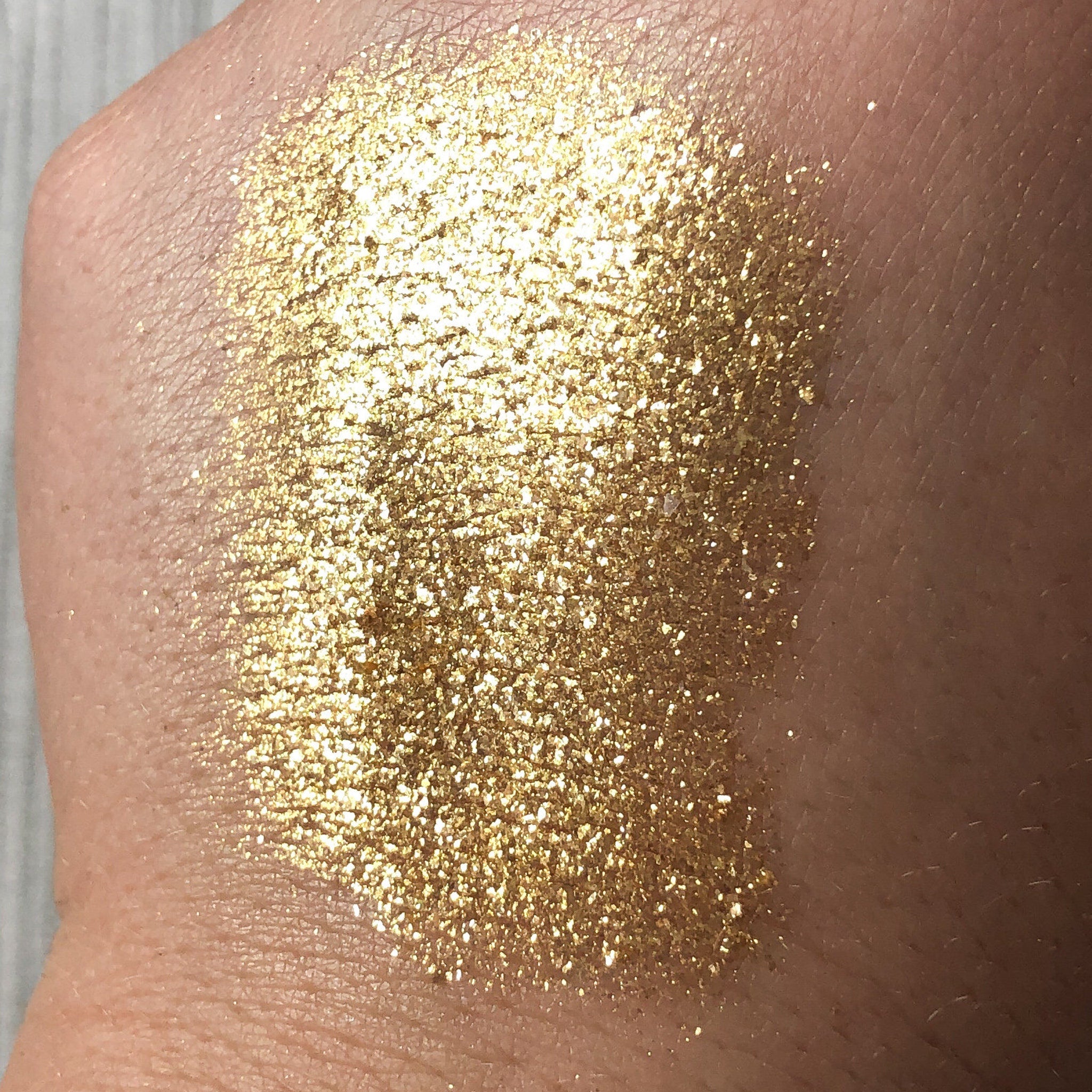 Gold glitter eyeshadow swatch on skin, showing metallic sparkle and texture