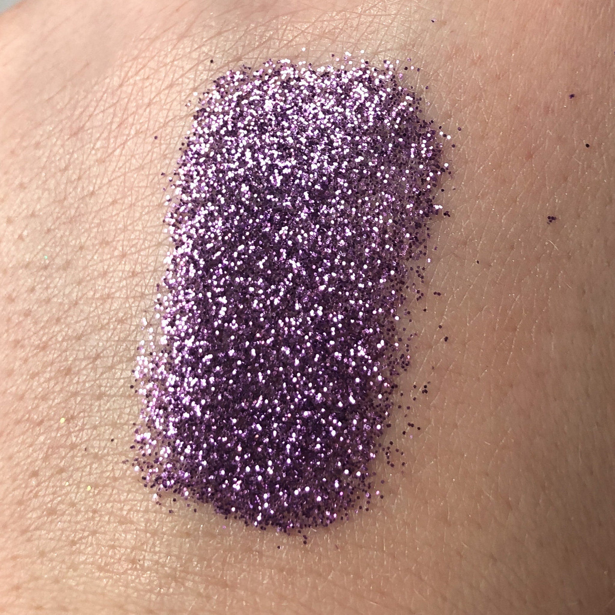 Purple glitter makeup swatch on skin, showing fine particles and texture