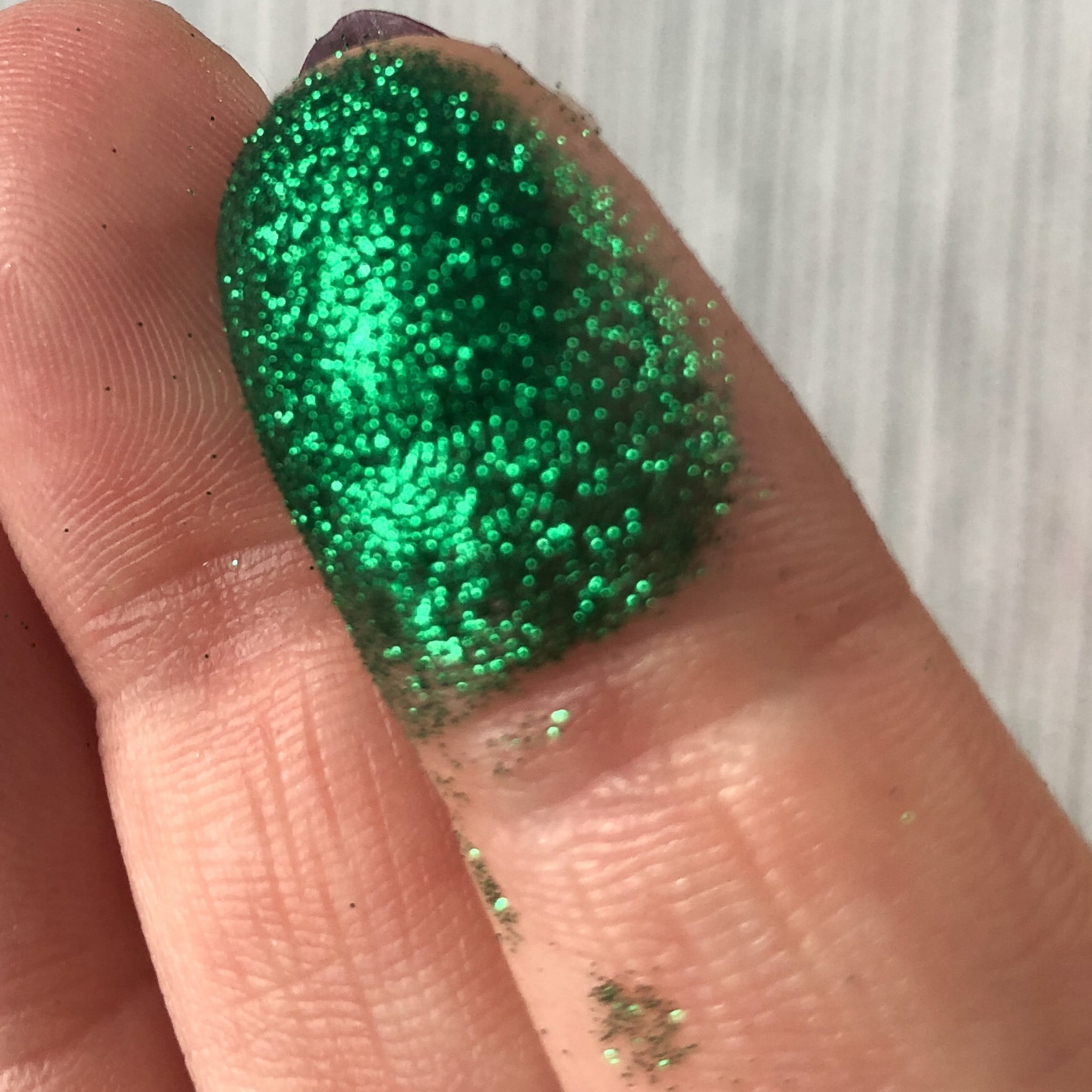 Green glitter on fingertip, sparkling texture, applied to skin
