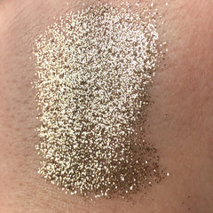 Close-up of golden glitter eye shadow pigment being applied with a fingertip for a shimmering halo effect