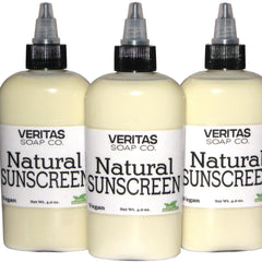 Natural sunscreen bottles with light yellow liquid, black caps, and white labels with Veritas Soap Co. text