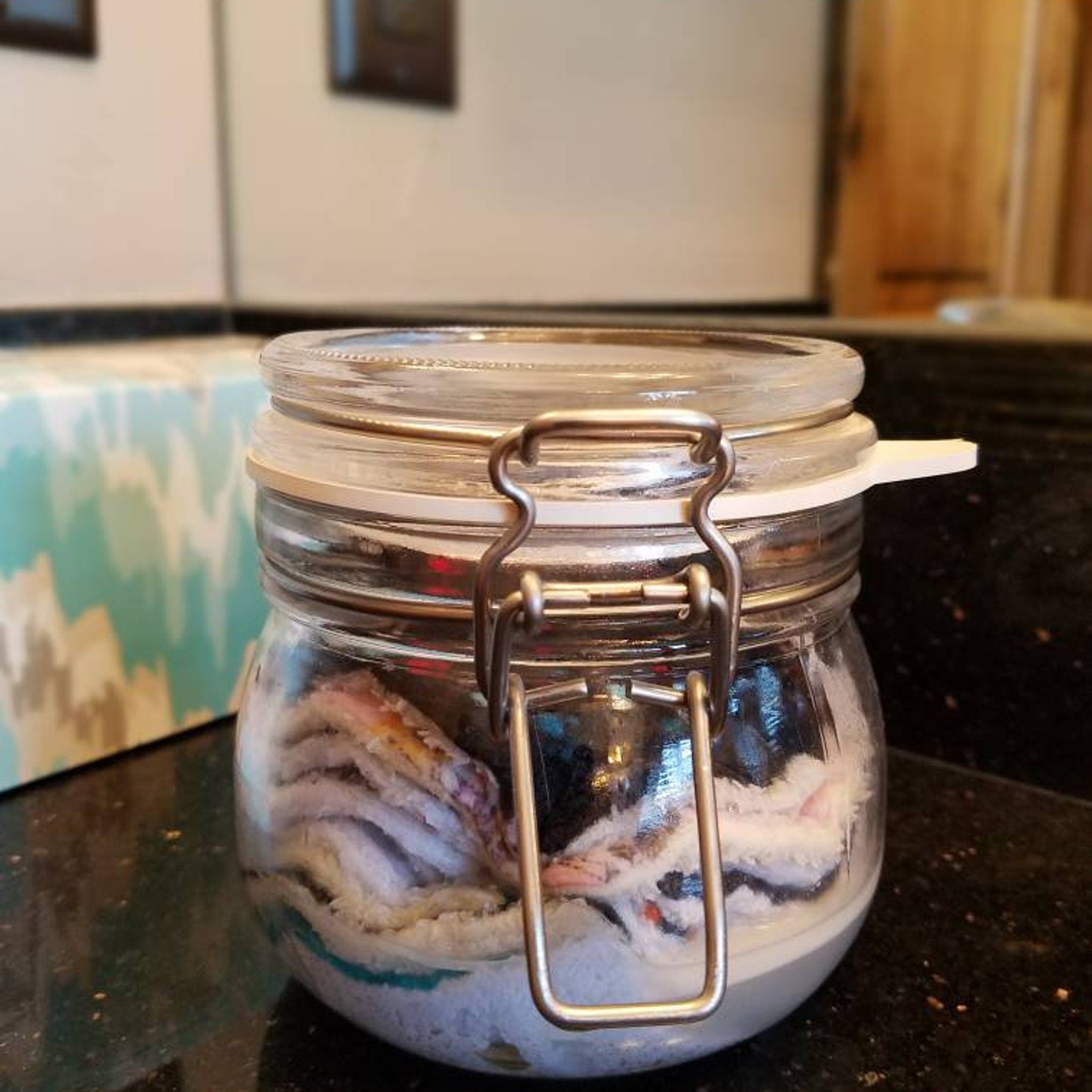 Glass jar with metal clasp, clear glass, and white lid with contents inside
