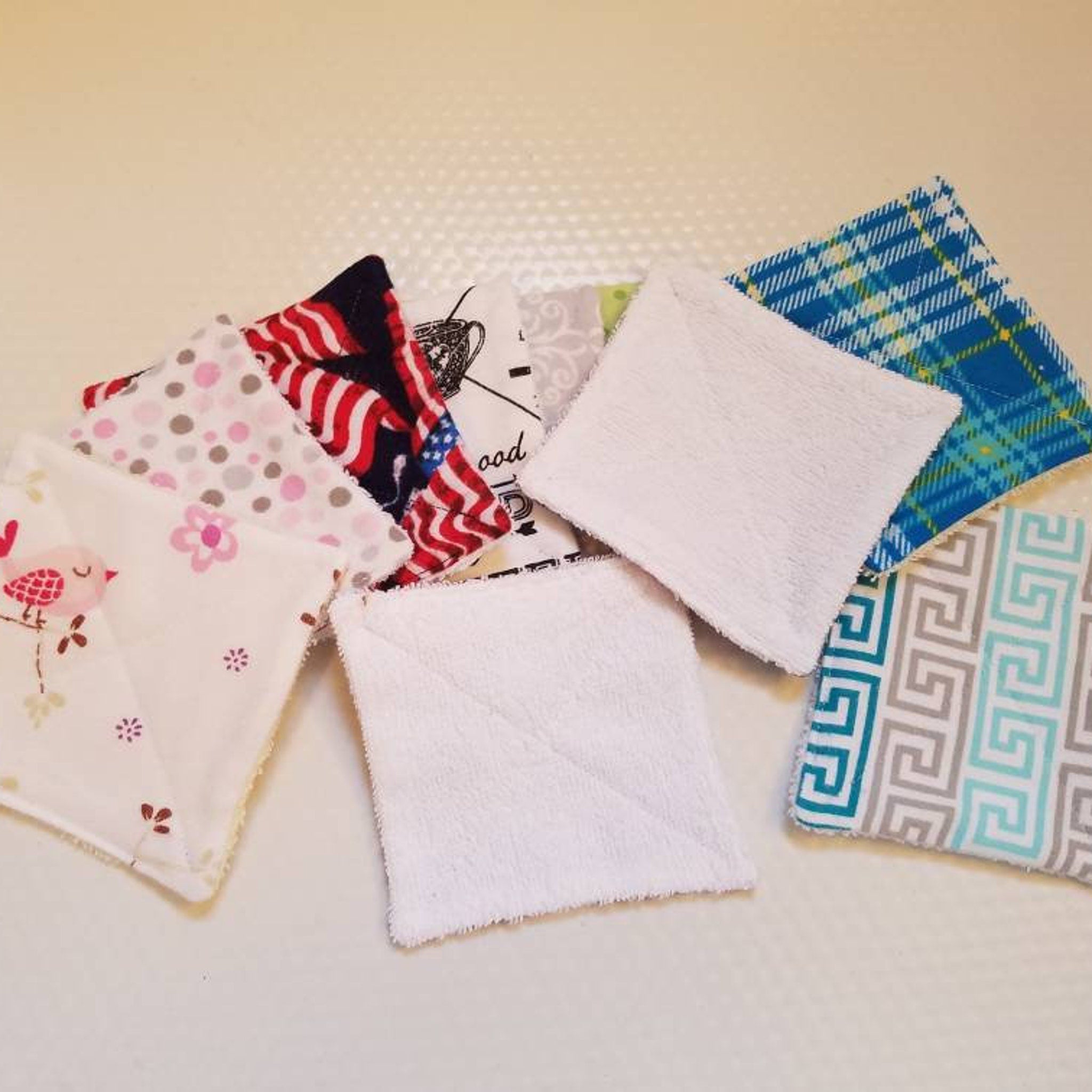 Reusable face cloths in various patterns and colors including white terry cloth, floral, and plaid designs