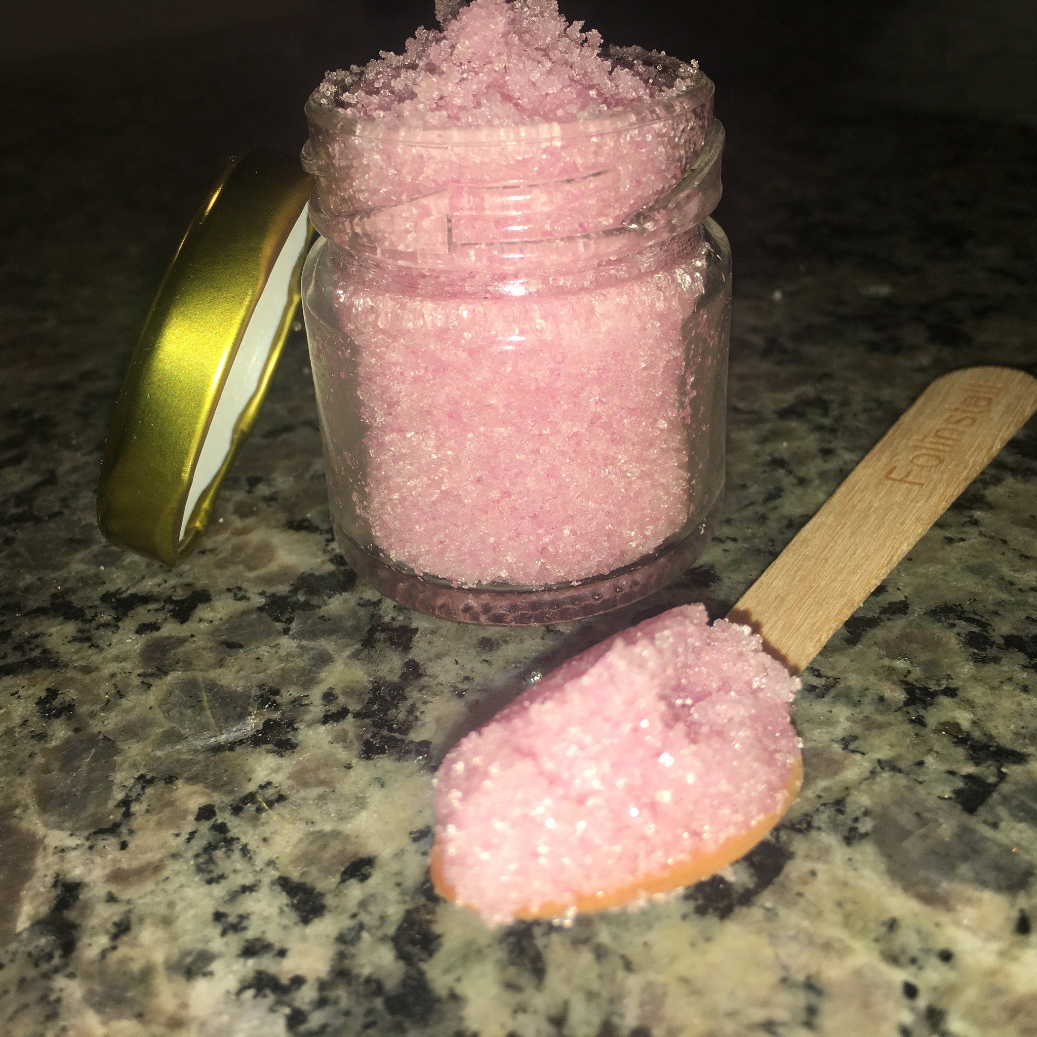 Pink sugar scrub in clear glass jar with gold lid and wooden spoon, Folinstall text visible